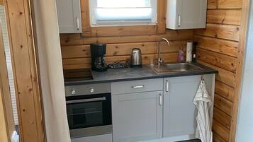 A compact kitchen with wooden walls, a window, a sink, and a stove.