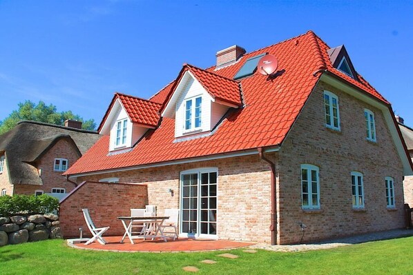 A two-story house with a red-tiled roof, a brick exterior, and a patio with outdoor furniture. - Holiday home with 2 bedrooms (St.Peter-Ording)
