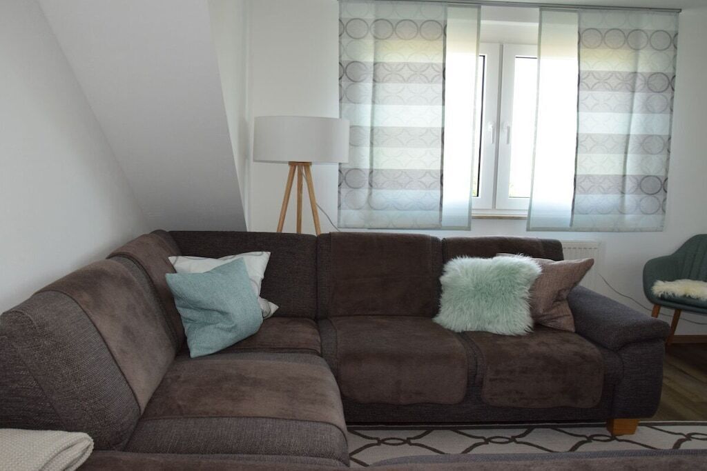 A living room with a brown sofa, a lamp, and a window with curtains.