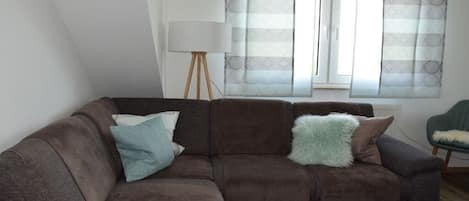 A living room with a brown sofa, a lamp, and a window with curtains.