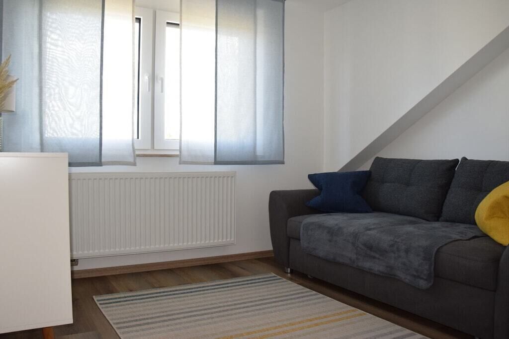 Ein Wohnzimmer mit einer Couch, einem Heizkörper, einem Fenster mit Vorhängen und einem Streifenmuster-Teppich.