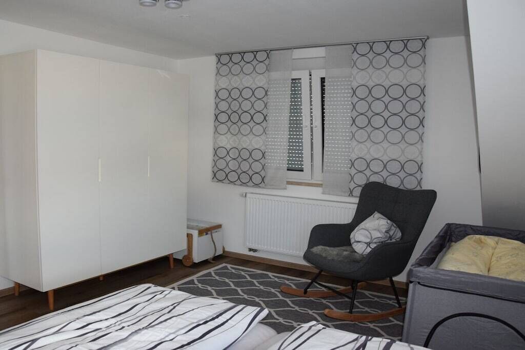 Une chambre avec une armoire, une chaise, un radiateur et une fenêtre ornée de rideaux à motifs.