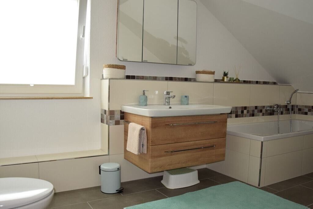 A bathroom with a toilet, a sink with a wooden vanity, a bathtub, and a window.