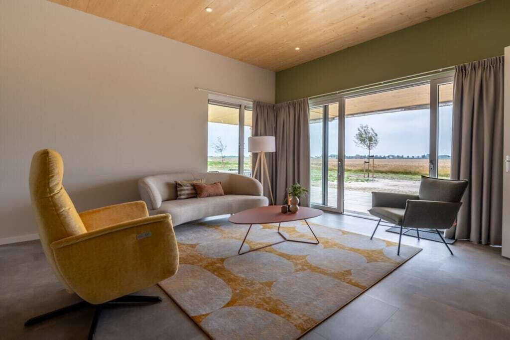 Een moderne woonkamer met een bank, fauteuils, een salontafel en uitzicht door grote ramen.