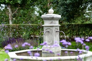 Ein steinerner Brunnen mit einem Wasserstrahl in der Mitte, umgeben von einer kreisförmigen Vertiefung.