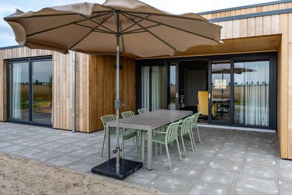 An outdoor patio with a table and chairs, a large umbrella, and wooden walls. - Holiday home with 1 bedroom (Zonnemaire)