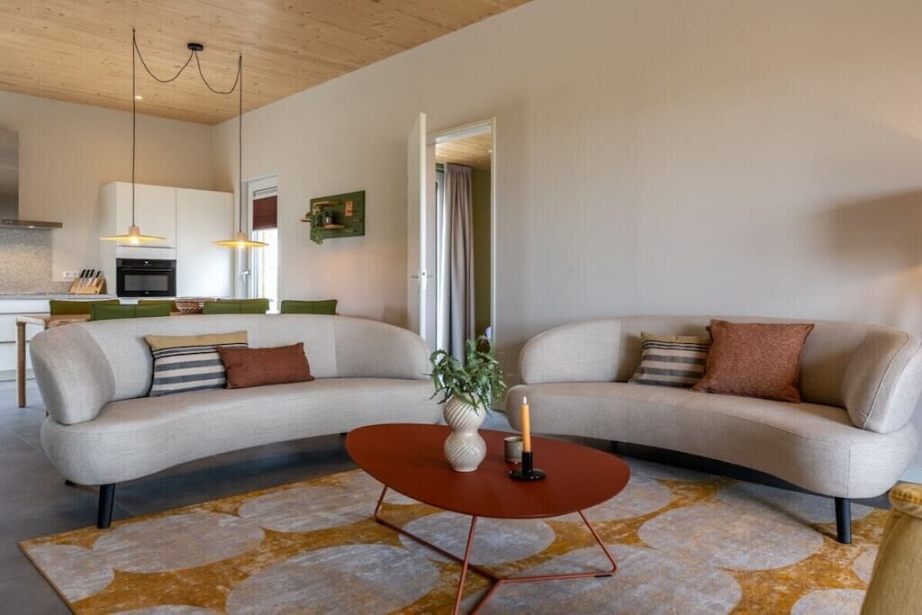 Un salon moderne avec un canapé aux lignes courbes, une table basse et une cuisine en arrière-plan.