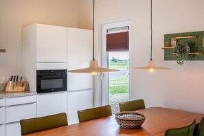 A modern kitchen with white cabinets, a built-in oven, a dining table with chairs, and pendant lighting. - Holiday home with 1 bedroom (Zonnemaire)