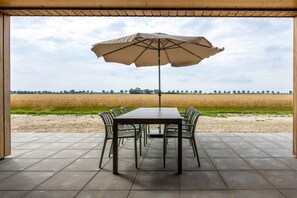 An outdoor patio with a table and chairs, an umbrella, and a view of a field. - Holiday home with 1 bedroom (Zonnemaire)