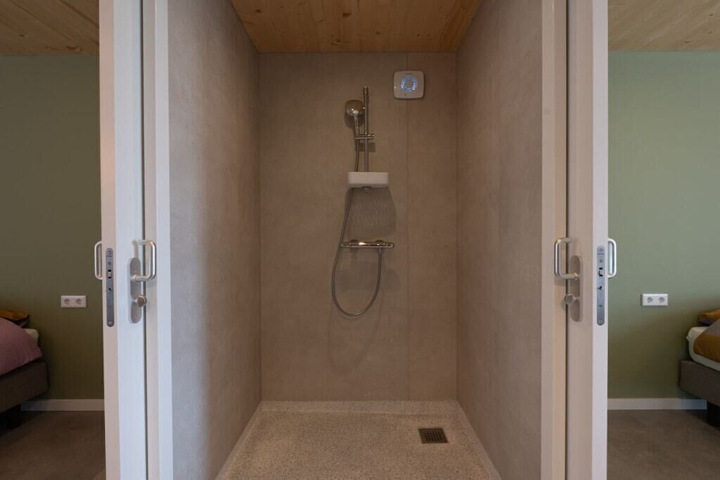 A walk-in shower with a handheld showerhead, a control panel, and a small shelf.