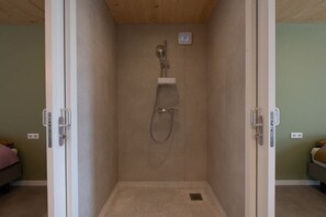 Eine bodenebene Dusche mit Handbrause, einer Bedienkonsole und einer kleinen Ablagefläche.