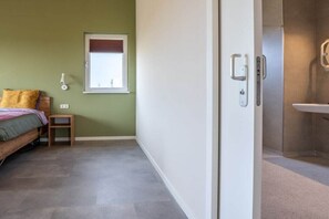 A bedroom with a bed, a small table, a window, and a bathroom with a sink. - Holiday home with 1 bedroom (Zonnemaire)