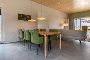 A modern dining area with a wooden table and green chairs, a sofa, and pendant lights. - Holiday home with 1 bedroom (Zonnemaire)