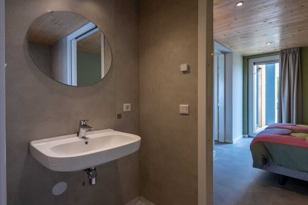 Un bagno con lavandino, specchio e vista su una camera da letto con un letto e tende.