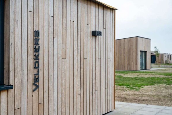 A building with vertical wooden panels and a black ventilation unit. - Holiday home with 1 bedroom (Zonnemaire)