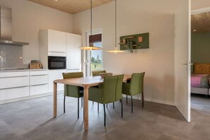 A modern kitchen with white cabinets, a wooden dining table, and green chairs. - Holiday home with 1 bedroom (Zonnemaire)