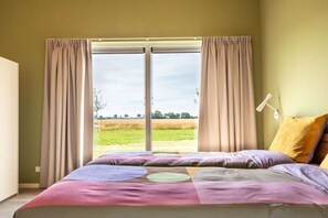 A bedroom with a large bed, curtains, a view of the outdoors, and a bedside lamp. - Holiday home with 1 bedroom (Zonnemaire)