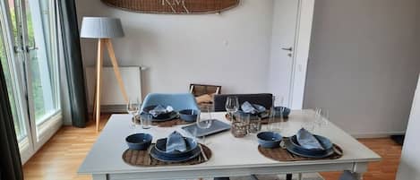 Ein Essbereich mit einem weißen Tisch, gedeckten Plätzen für vier Personen, blauem Geschirr und einem Wandbild.