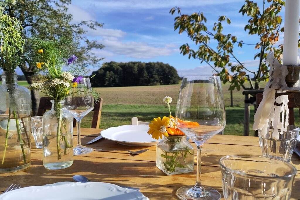 A table set outdoors with clear glassware, a white plate, and a vase with flowers.