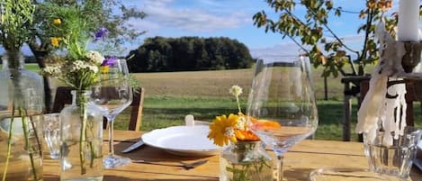 Ein Tisch draußen gedeckt mit klarem Glasgeschirr, einem weißen Teller und einer Vase mit Blumen.