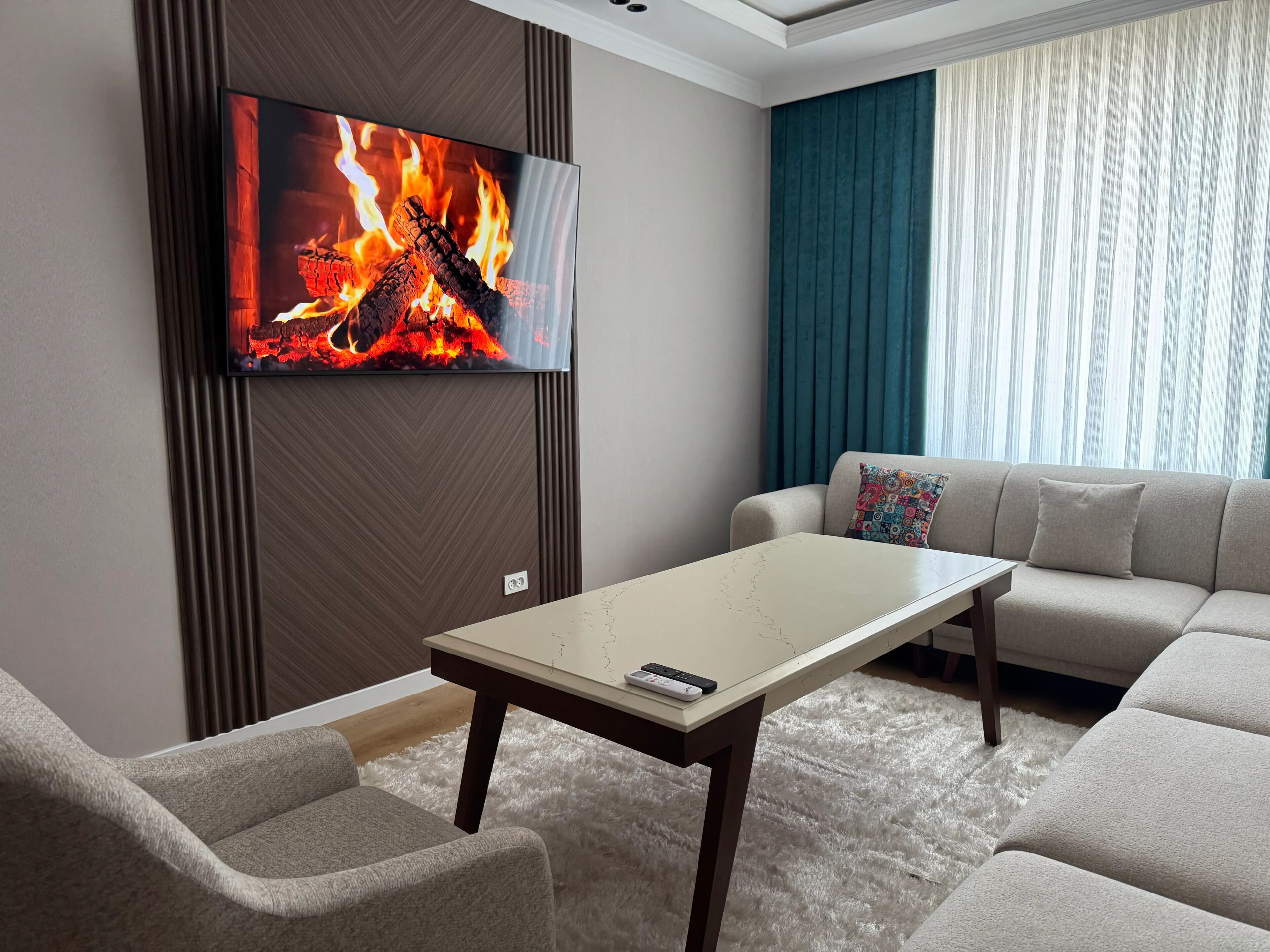 Un salon moderne doté d’un téléviseur à écran plat diffusant une image de feu, d’un canapé, d’une table basse et d’un coussin décoratif à motifs.