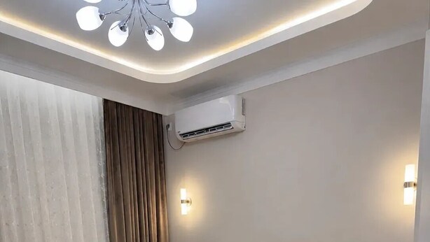 Una habitación de hotel con cama, mesitas de noche, aire acondicionado de pared y lámpara en el techo.