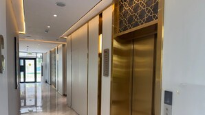 Un pasillo con piso brillante, un ascensor empotrado en la pared y una puerta que da al exterior.