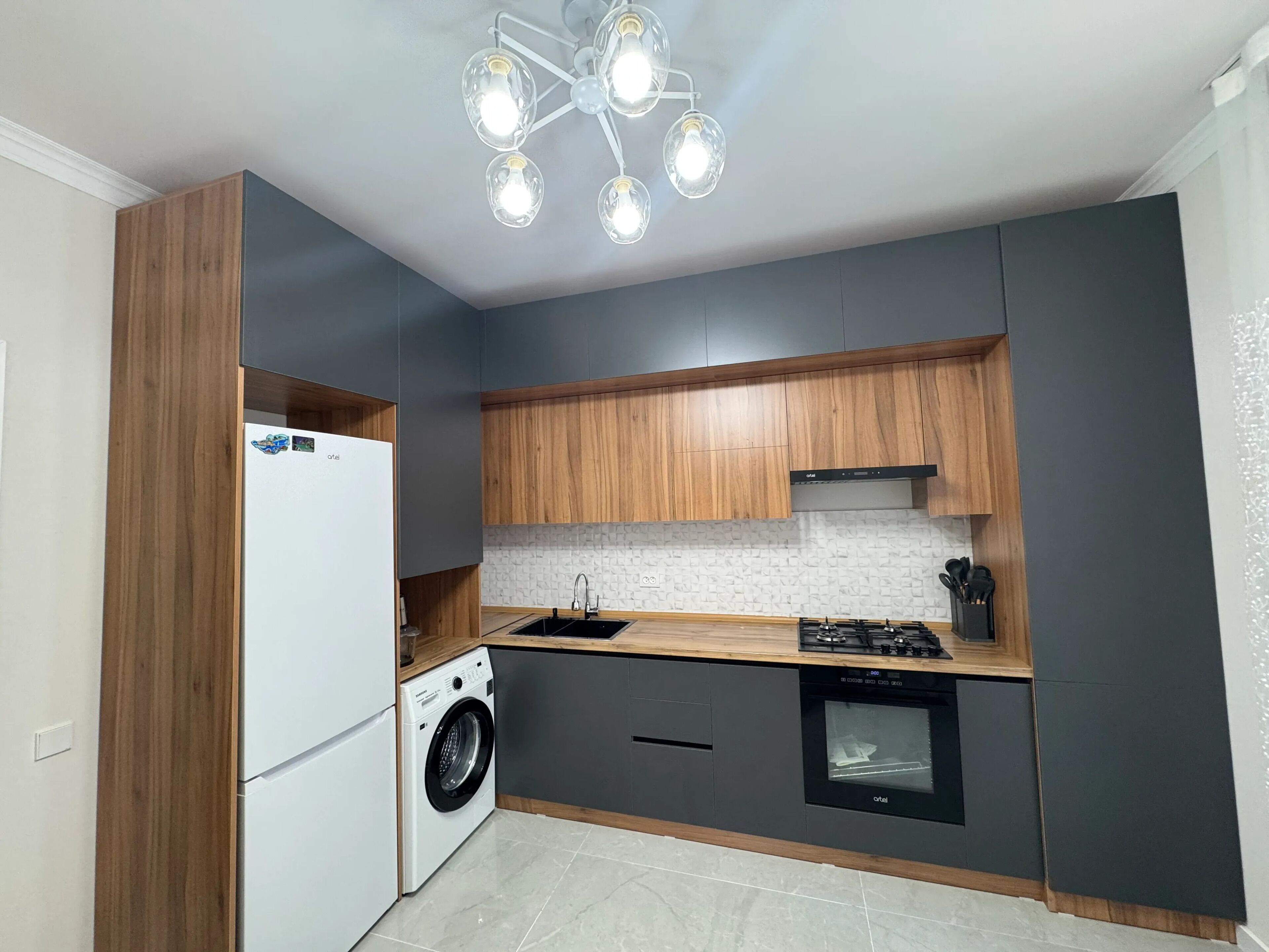 A compact kitchen with a built-in washer, a gas stove, and a modern light fixture.