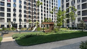 Un edificio residencial con varios balcones, un parque infantil con toboganes y estructuras para escalar, y un césped bien cuidado.