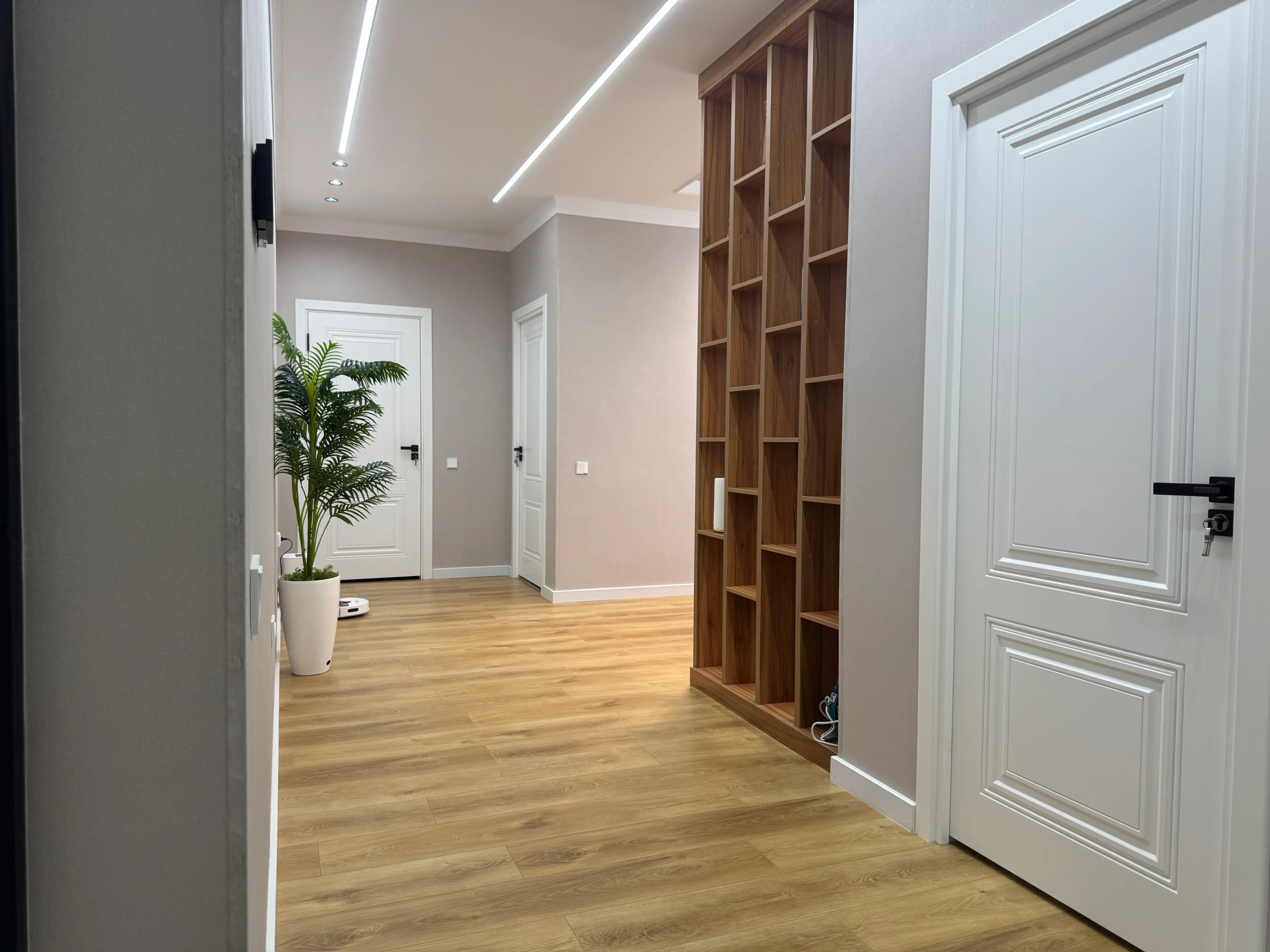 Un couloir doté d’un plancher en bois, de portes blanches et d’une bibliothèque intégrée en bois.