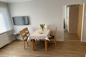 A dining area with a table, chairs, a flat-screen TV, and a vase with flowers.