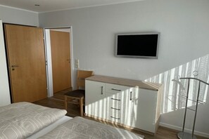 A bedroom with a bed, a desk with drawers, a chair, a wardrobe, and a TV mounted on the wall.
