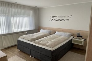 Un dormitorio con una cama doble, una mesita de noche con lámpara y una pared con una frase decorativa.