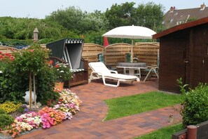 A patio with a grill, lounge chairs, and a garden with flowers.