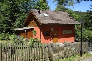 Ein kleines, eingeschossiges Holzhaus mit geneigtem Dach, einem Holzzaun und einem Lampenpfosten.
