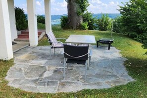 Eine Außenpatio mit Steinboden, zwei Korbstühle, einem Tisch und Blick auf die Landschaft.