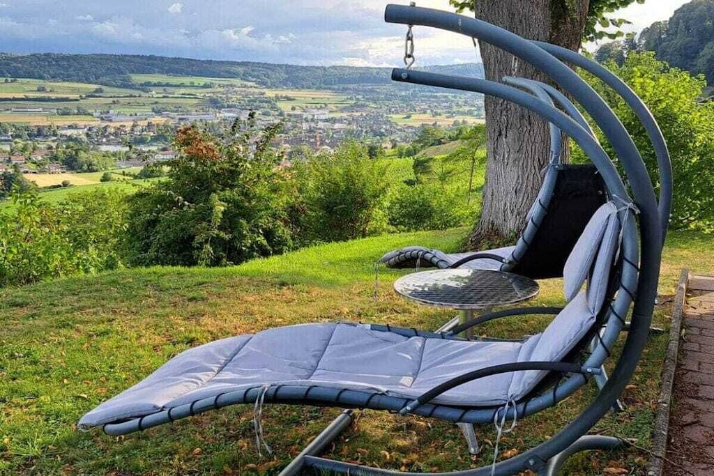 Ein Stuhl mit gepolstertem Sitz und Rücken, draußen platziert mit Blick auf eine Stadt und Hügel im Hintergrund.