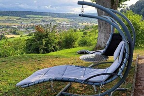 A chair with a cushioned seat and back, positioned outdoors with a view of a town and hills in the background. - Country house Bleiki (Stone on the Rhine)