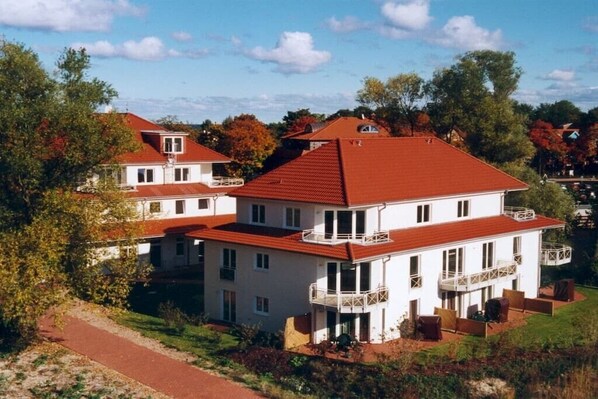 A multi-story residential building with a red roof, multiple balconies, and a pathway leading to the entrance. - Holiday apartment with 2 bedrooms (Boltenhagen)