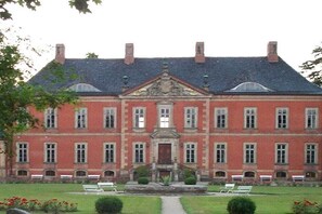 A large, symmetrical building with a central entrance, multiple windows, and a formal garden with benches. - Holiday apartment with 2 bedrooms (Boltenhagen)