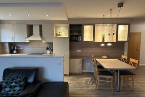 A modern kitchen with built-in appliances, a dining area with a wooden table and chairs, and a seating area with a sofa. - Holiday apartment with 2 bedrooms (Boltenhagen)