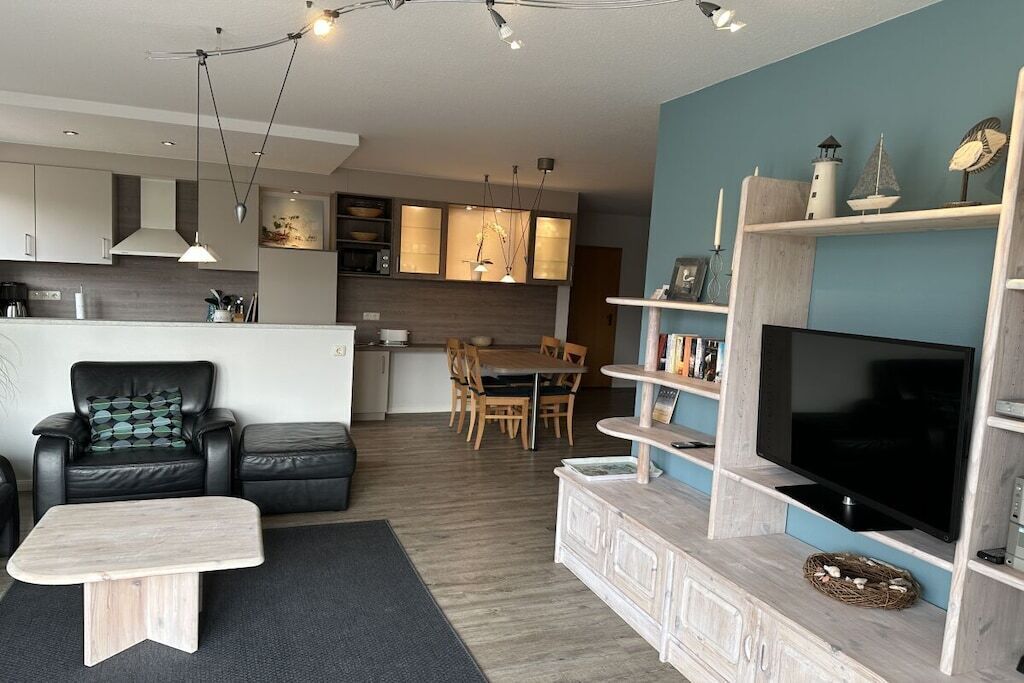 A modern living room with a flat-screen TV, a sofa, a coffee table, and a dining area in the background.