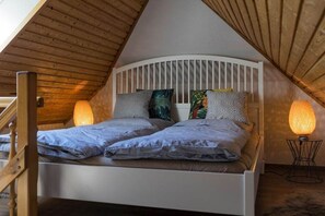 A loft-style bedroom with a sloped ceiling, a white bed with multiple pillows, and a floor lamp. - Holiday apartment with 1 bedroom (Malchow)