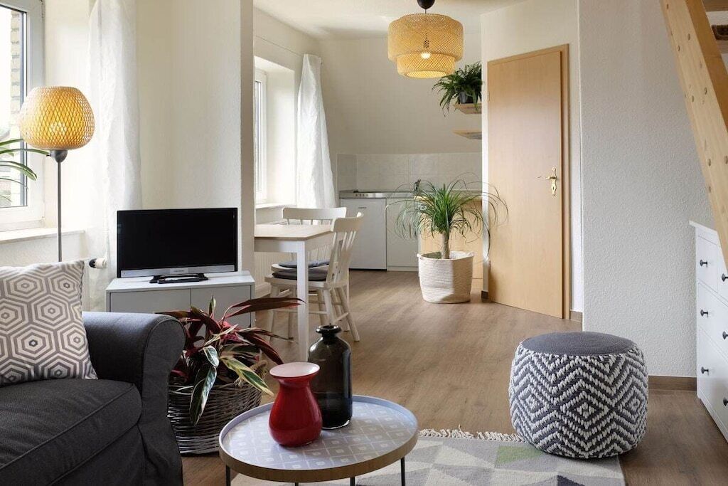 A modern living room with a sofa, a round coffee table, and a television. There is a kitchen area in the background with a dining table and chairs.