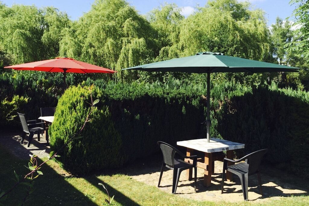 An outdoor patio with a table and chairs, two umbrellas, and a hedge in the background.