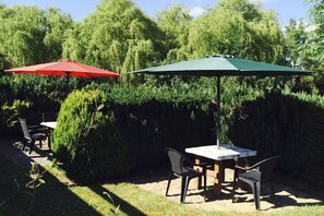 An outdoor patio with a table and chairs, two umbrellas, and a hedge in the background. - Holiday apartment with 1 bedroom (Malchow)