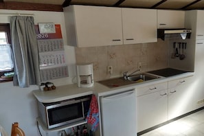 A kitchen with white cabinets, a microwave, a coffee maker, and a calendar. - Dune House Holiday Park Duinendaele (De Panne-Adinkerke)