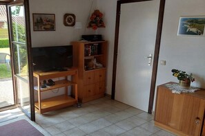 A room with a television, wooden shelves, a cabinet, and a door leading outside. - Dune House Holiday Park Duinendaele (De Panne-Adinkerke)