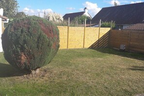 Ein von einer Hecke und einem Holzzaun umgebener Garten, mit einem Haus und einem Ziegeldach.