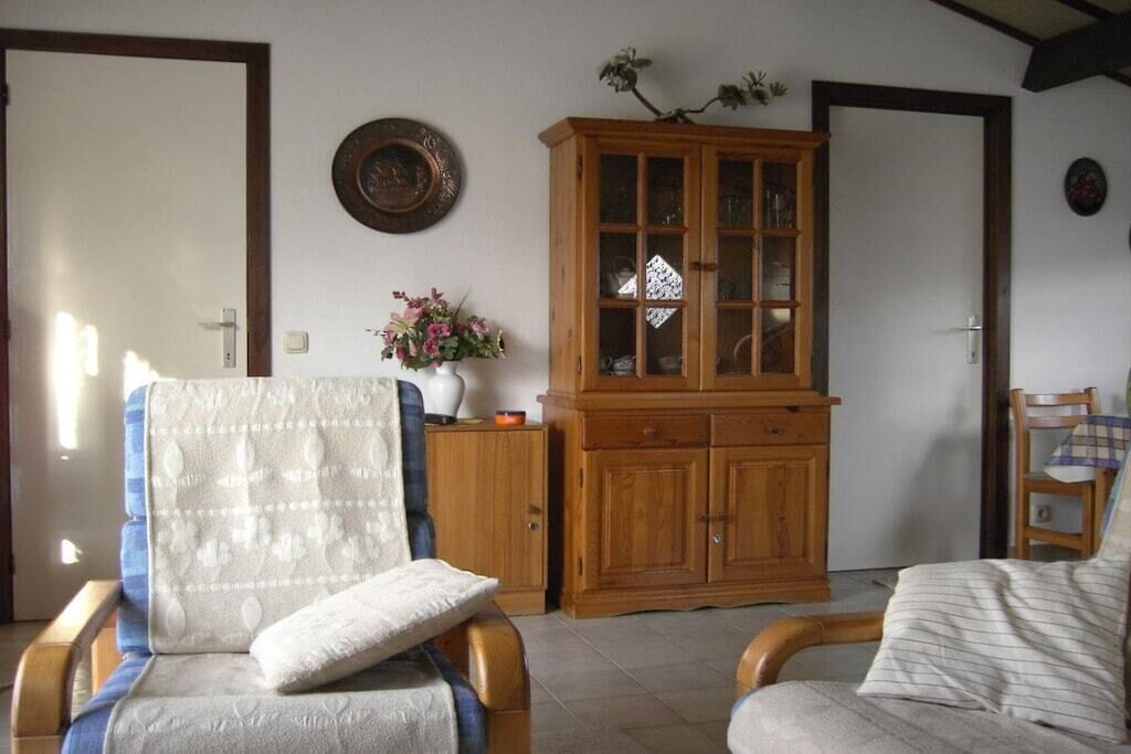 Une pièce comprenant un meuble en bois, une chaise avec un coussin et une petite table sur laquelle est posé un vase de fleurs.